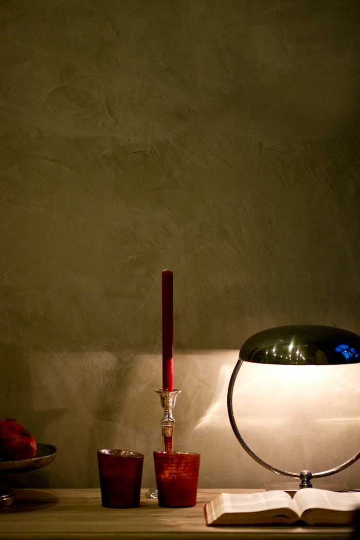 A stylish indoor setting featuring a lit candle, vintage lamp, and open book on a wooden table.
