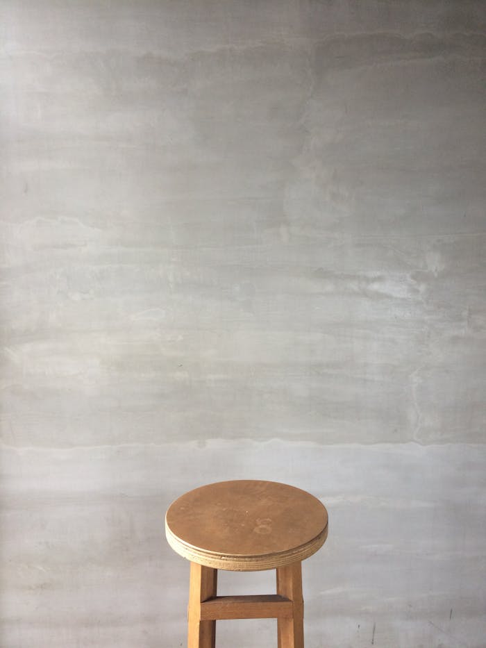 A minimalist wooden stool placed against a light grey wall, ideal for interior design concepts.