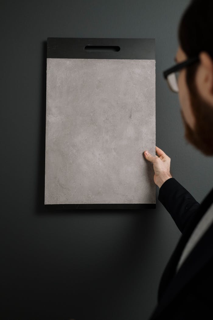 our-mission A man holds a textured sample board against a dark wall. Vertical shot.